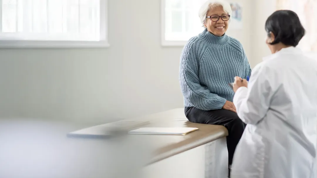 An older female patient talking to a female physician in an exam room.