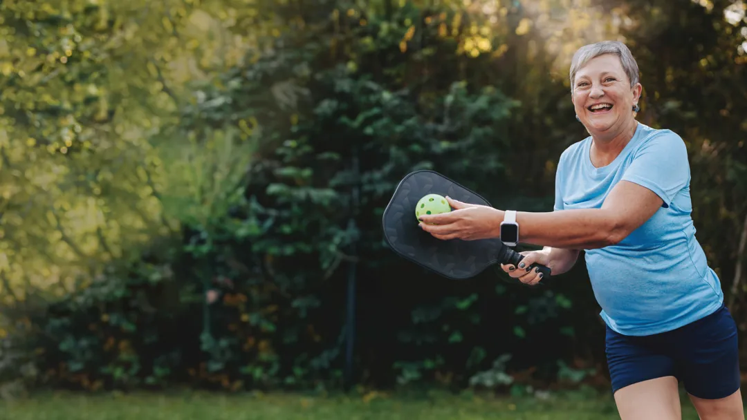 An older woman playing pickleball outdoors.