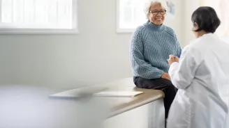 An older female patient talking to a female physician in an exam room.