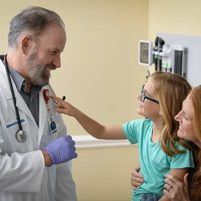 Child sitting on her mother's lap and pointing at doctor's AdventHealth heart badge