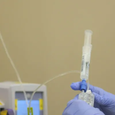 Gloved hands hold up a syringe of bamlanivimab