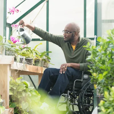 Man in wheelchair in a greenhouse watering a plant.