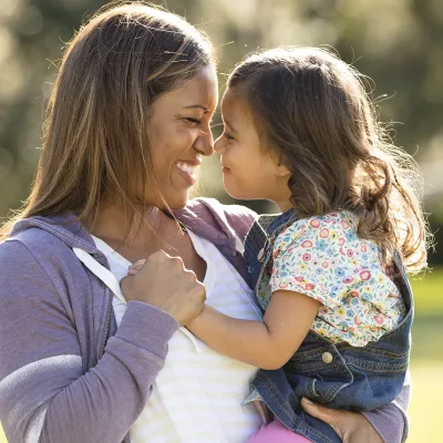 Mother and elementary-aged daughter giving eskimo kisses in the park. 