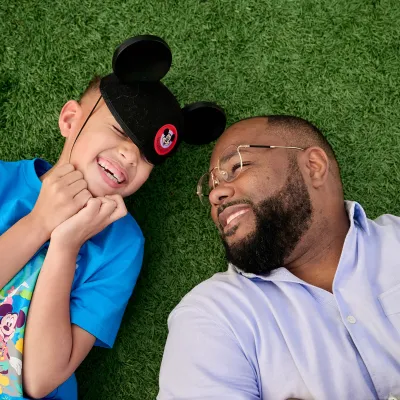 Father with child Wearing Mickey Mouse hat lying on grass.