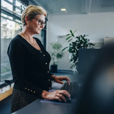 A Woman Stands at a Stand Up Desk in Her Office by a Window.