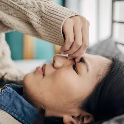 A Woman Squeezes the Bridge of Her Nose While Laying Down at Home