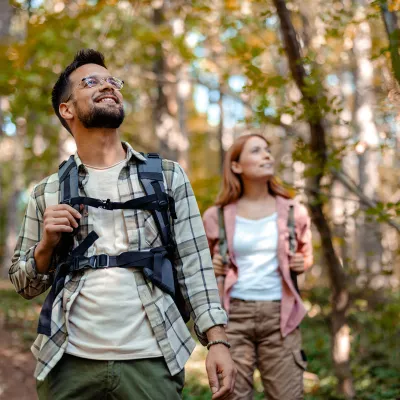 A man and woman with backpacks walking in the woods.