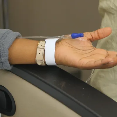 Woman's arm on a chair with infusion needle bandaged onto her wrist 