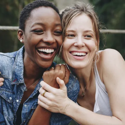 Two women, holding each other and grasping hands, smiling and laughing.