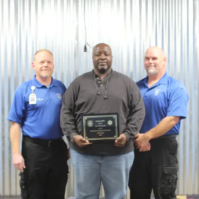 Three men standing next to each other, the man in the middle is holding an award.
