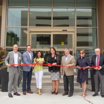 7 people prepare to cut red ribbon in front of new behavioral health building