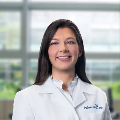 Amanda Robinson, DO, smiles at the camera. She is a white woman with brunette hair and is wearing a white medical coat.