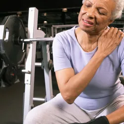 An older woman holds her shoulder in pain.