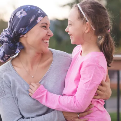 A mother and cancer survivor is sitting, with one arm around her daughter.