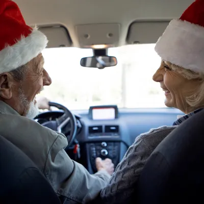 Older couple sitting in a car while wearing Santa hats.