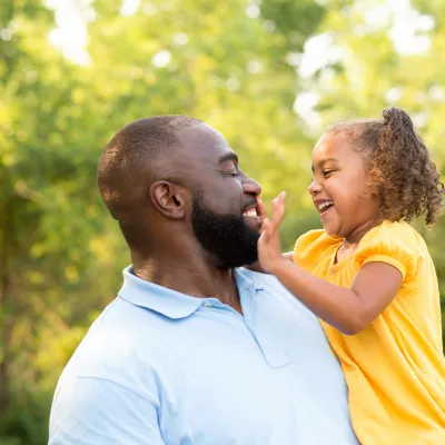 African-American father holding his African-American daughter with her hand in his face while in the forest