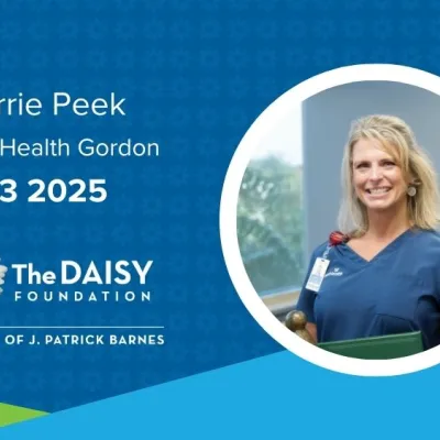 Carrie Peek, a white, blonde woman wearing blue scrubs, stands with her DAISY Award certificate and statue.