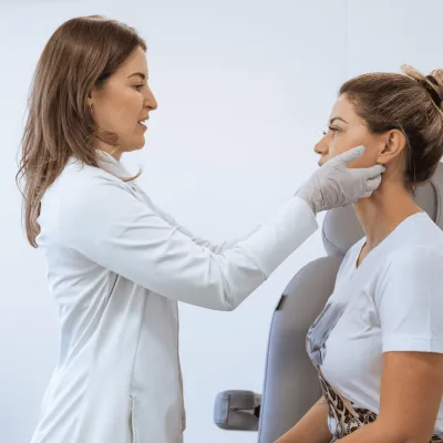 Dermatologist examining female patient's face in room