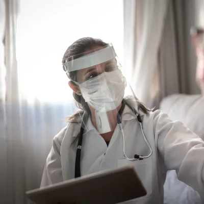 Doctor wearing PPE and talking with a patient that's wearing a mask.