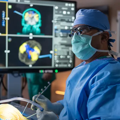 Surgeon at AdventHealth operating on a patients brain. A series of brain scans are located on the monitor behind him.