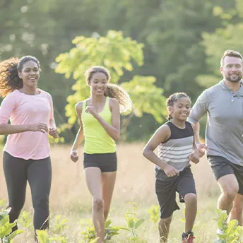 A family of four, running together outside in a field.