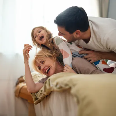 A mother and father play with their child in a bedroom.
