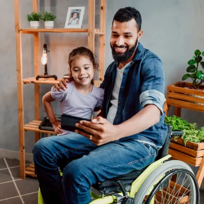 A father in a wheelchair taking a selfie photo with his young daughter.
