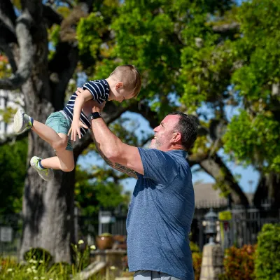 An older father playfully lifts his son in the air