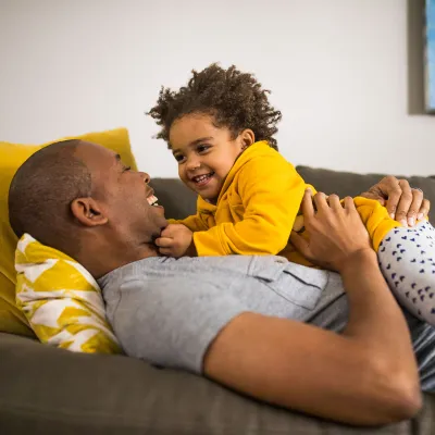A dad is embracing his baby while they are laying down on the couch.