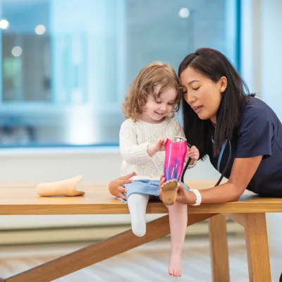A medical professional helping a little girl put on a prosthetic leg