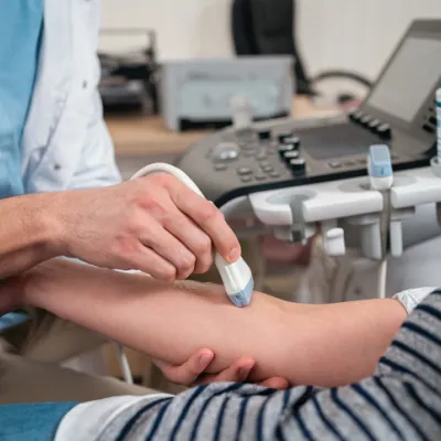 At the medical clinic, unrecognizable Caucasian male doctor doing the doppler ultrasound test evaluation of arteries and veins on a senior female patient