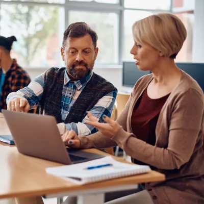 Adult students talking while using laptop and studying together in the classroom.