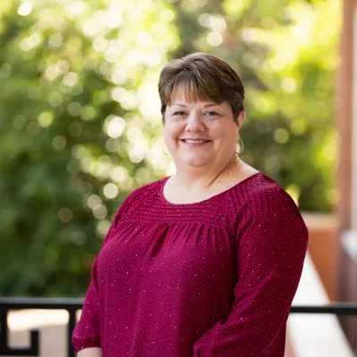 Laurie Chandler, a white woman with short brown hair and wearing a burgundy top, smiles at the camera.  The background appears to be a blurred, outdoor porch setting.