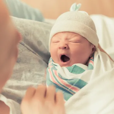A mom carrying her new born baby. The new new born baby is yawning