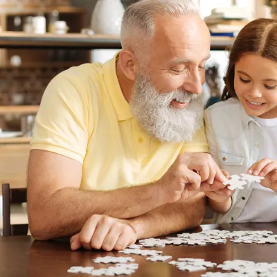 A grandfather puts together a puzzle with his granddaughter. 