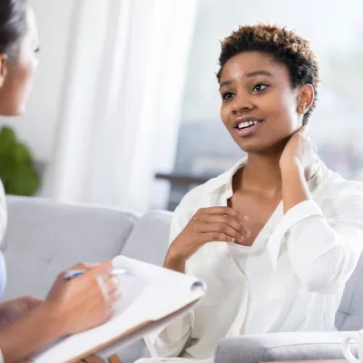 A young woman rubs her neck as she talks to a nurse