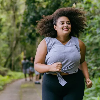 Hispanic woman running outdoors in a forest.