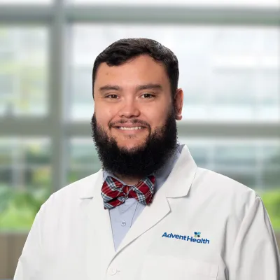 Jacob Parker, a dark-haired, bearded white man in a white medical coat, stands smiling in front of a blurred office-style background.