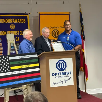 EMT Jared Firestone accepts his award from Marty Robinson and an unnamed representative of the Noon Optimist Club of Rome