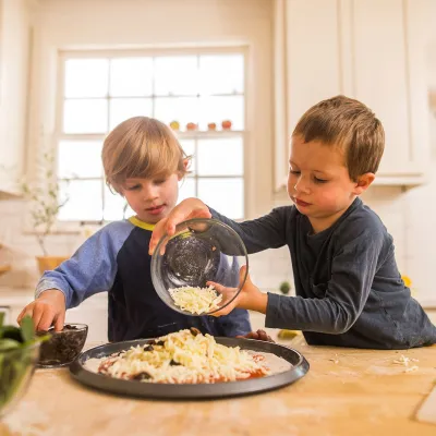 A boy making a veggie pizza with his brother. 
