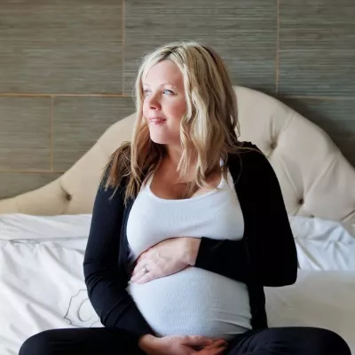 Pregnant woman sitting on bed holding belly
