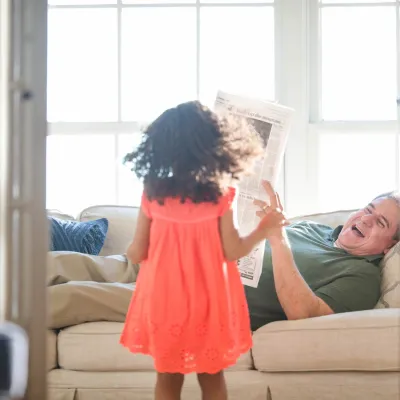 Father laying on sofa reading newspaper with his daughter. 