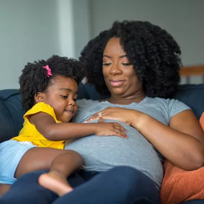 A mother having her daughter touch and feel her baby belly