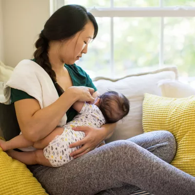 A mother breast-feeding her baby in the couch.