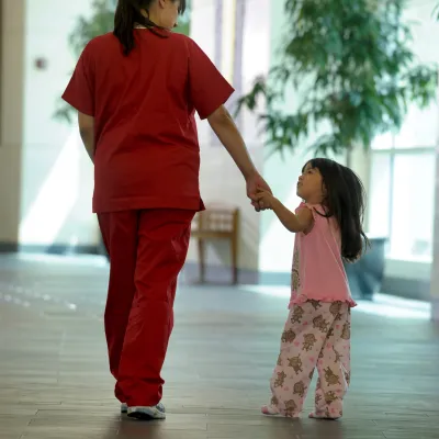 A nurse walks a child patient to her room.