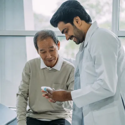 An older patient looking at medical equipment with his physician.