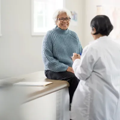 An older female patient talking to a female physician in an exam room.