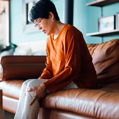 A woman sits on a couch and hold her hand to her leg.