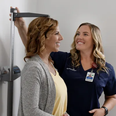 A Primary Care+ Nurse Measures the Height of a Smiling Patient