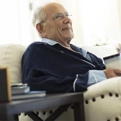 Elderly man sitting on couch drinking coffee.